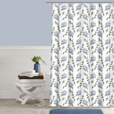 a white shower curtain with blue flowers and green leaves on it next to a bath tub