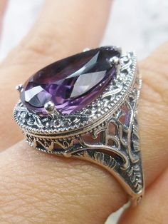 Natural Amethyst Gemstone Teardrop RingTear Vic Design#D28 Inspired by Victorian and Art Deco designs, this high-quality filigree ring is handcrafted in sterling silver. This teardrop ring is set with an 8.37 carat pear cut flawless natural purple amethyst gemstone. The gem is 16mm (~5/8") x 12mm (~1/2"). The gorgeous stones have lovely vibrant color. The inside of the band is marked 925 for sterling silver. Notice the beautiful filigree of the silver setting. This is a ring with beauty and grac Silver Amethyst Pear-shaped Jewelry, Silver Pear-shaped Amethyst Jewelry, Pear-shaped Amethyst Silver Jewelry, Classic Teardrop Jewelry With Intricate Design, Elegant Teardrop Amethyst Gemstone Ring, Elegant Silver Teardrop Amethyst Ring, Elegant Teardrop Amethyst Ring, Filigree Drop Jewelry For Anniversary, Elegant Teardrop Amethyst Ring Gift