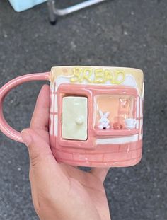 a hand holding a pink coffee mug with the word bread on it's side