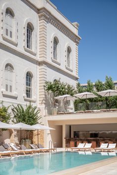 an outdoor swimming pool with lounge chairs and umbrellas in front of a large white building