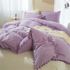 an unmade bed with purple sheets and pillows