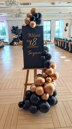 black and gold balloons are stacked on an easel in the center of a room