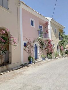 a pink house with blue shutters and flowers on the side of the street in front of it