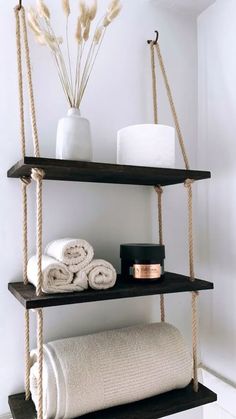 two shelves with towels and candles on them in a bathroom, one shelf is made out of wood and the other has rope