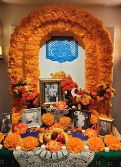 a table topped with orange flowers and pictures next to an arch covered in fake flowers