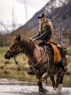 a woman riding on the back of a brown horse across a river