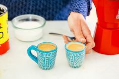 two coffee mugs sitting on top of a table next to a blender and measuring cup