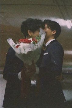 two people kissing each other with flowers in front of an airplane wing and one person wearing a suit