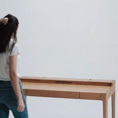 a woman standing next to a wooden table with a drawer on it's side