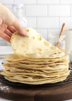 a stack of tortillas being held up by a person's hand over a cooling rack