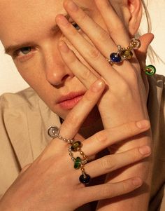 a woman is holding her hands to her face while wearing rings and bracelets on her fingers