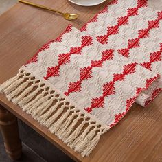 a red and white table runner sitting on top of a wooden table next to a plate