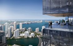 a man standing on top of a tall building next to a body of water with buildings in the background