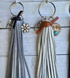 three tasseled key chains hanging from hooks on a white wooden wall with a flower