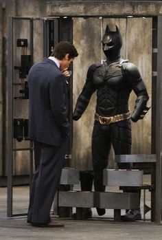 two men in suits standing next to each other near a batman statue and another man wearing a suit