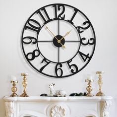 a clock that is on the wall above a mantle with candles and figurines