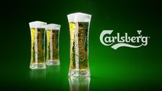 three tall glasses filled with beer sitting on top of a green table next to a logo