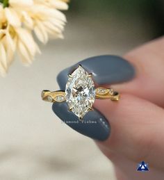 a woman's hand holding a ring with a large diamond on the side and a flower in the background