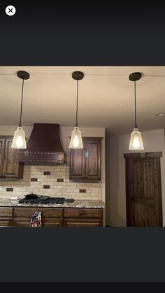 three lights hanging from the ceiling in a kitchen with wood cabinets and marble counter tops