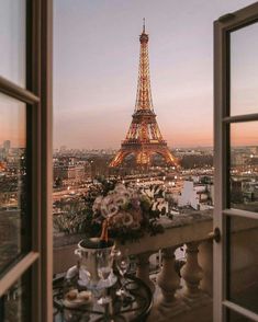 the eiffel tower is lit up at night from an open window with flowers