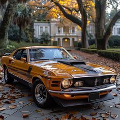 an orange muscle car parked in front of a house with trees and leaves on the ground