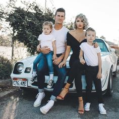 a man, woman and two children sitting on the hood of a car