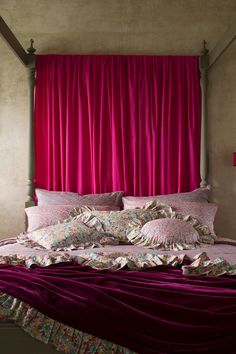 a bed with pink sheets and pillows in front of a red curtain