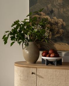 there is a vase with flowers and fruit on the sideboard in front of it