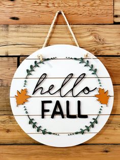 a white sign that says hello fall hanging on a wooden wall with leaves around it