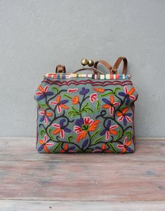 a purse sitting on top of a wooden table next to a gray wall with flowers painted on it