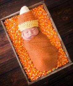 a newborn baby wearing a knitted hat and sleeping on corn kernels in a wooden crate