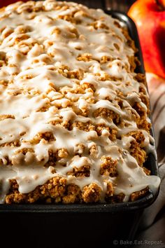 a close up of a cake in a pan with icing and apples behind it