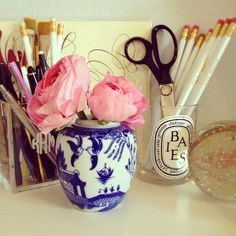 a blue and white vase with pink flowers in it next to pens and pencils