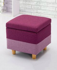 a purple ottoman with wooden legs in front of a brick wall