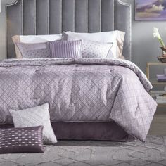 a bed with purple comforter and pillows on top of it in a gray room