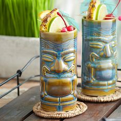 two tiki glasses sitting on top of a wooden table