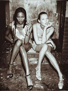 two young women sitting on a bench in front of a building with graffiti all over it