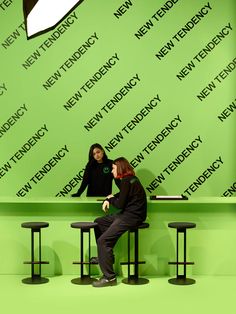 two people sitting on stools in front of a green wall with the words new technology