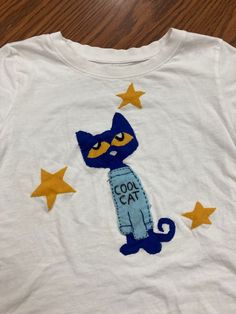 a white t - shirt with a blue cat and stars on the front that says cool cat