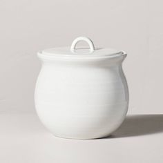 a large white pot with a lid on the side, sitting on a plain surface