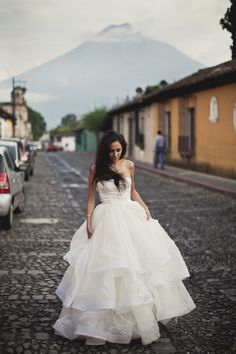 a woman in a white wedding dress walking down the street with cars parked on both sides