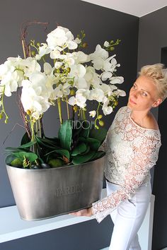 a woman holding a potted plant with white flowers in it and posing for the camera