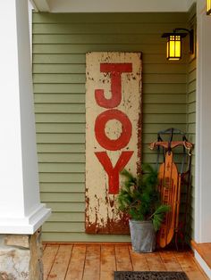 a sign that says joy hanging on the side of a house next to a potted plant