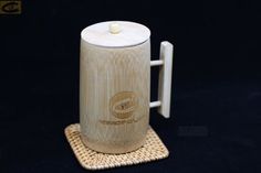 a wooden coffee mug with a white lid and handle on a woven place mat in front of a black background