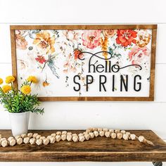 a sign that says hello spring with flowers in front of it and a potted plant next to it