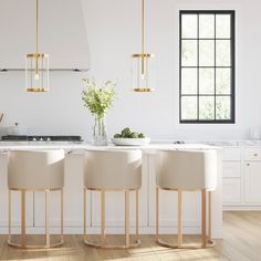 three white stools are in front of a kitchen island with marble counter tops and gold accents