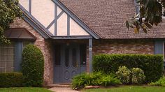 a house with a clock in front of it and bushes around the yard area next to it