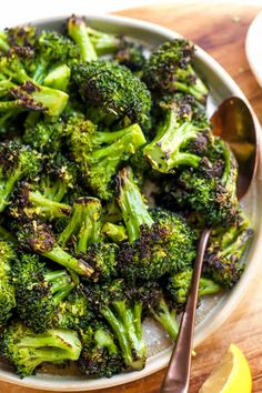 a white bowl filled with broccoli on top of a wooden table next to lemon wedges