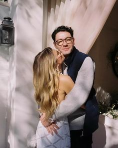 a man and woman kissing in front of a white wall