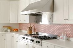 a kitchen with white cabinets and pink tile backsplashes on the wall above the stove